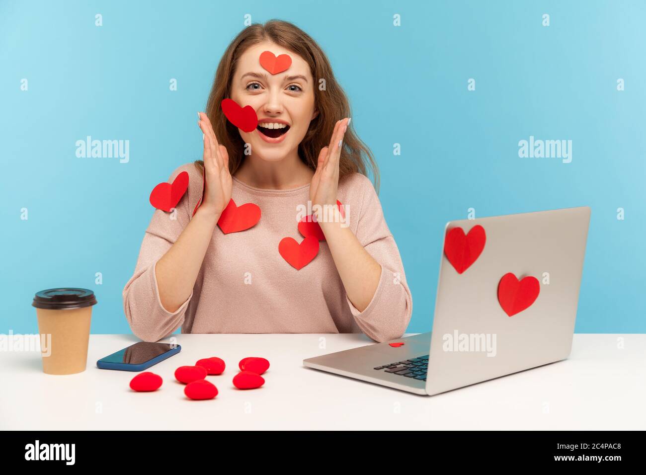 Amazed joyful young woman sitting all covered with sticker love hearts, looking at camera with surprised expression, full of valentine's day greetings Stock Photo