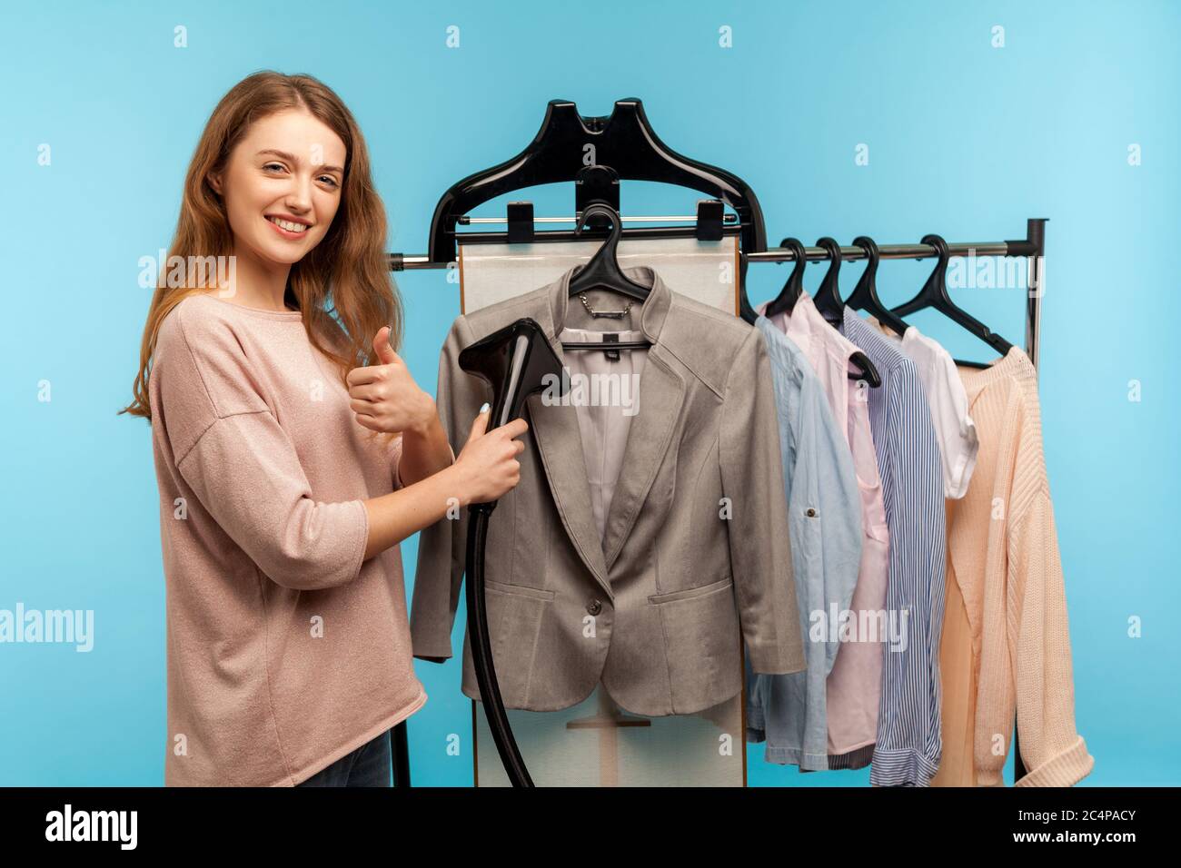 Satisfied housewife steaming business suit at drycleaner and showing thumbs up,