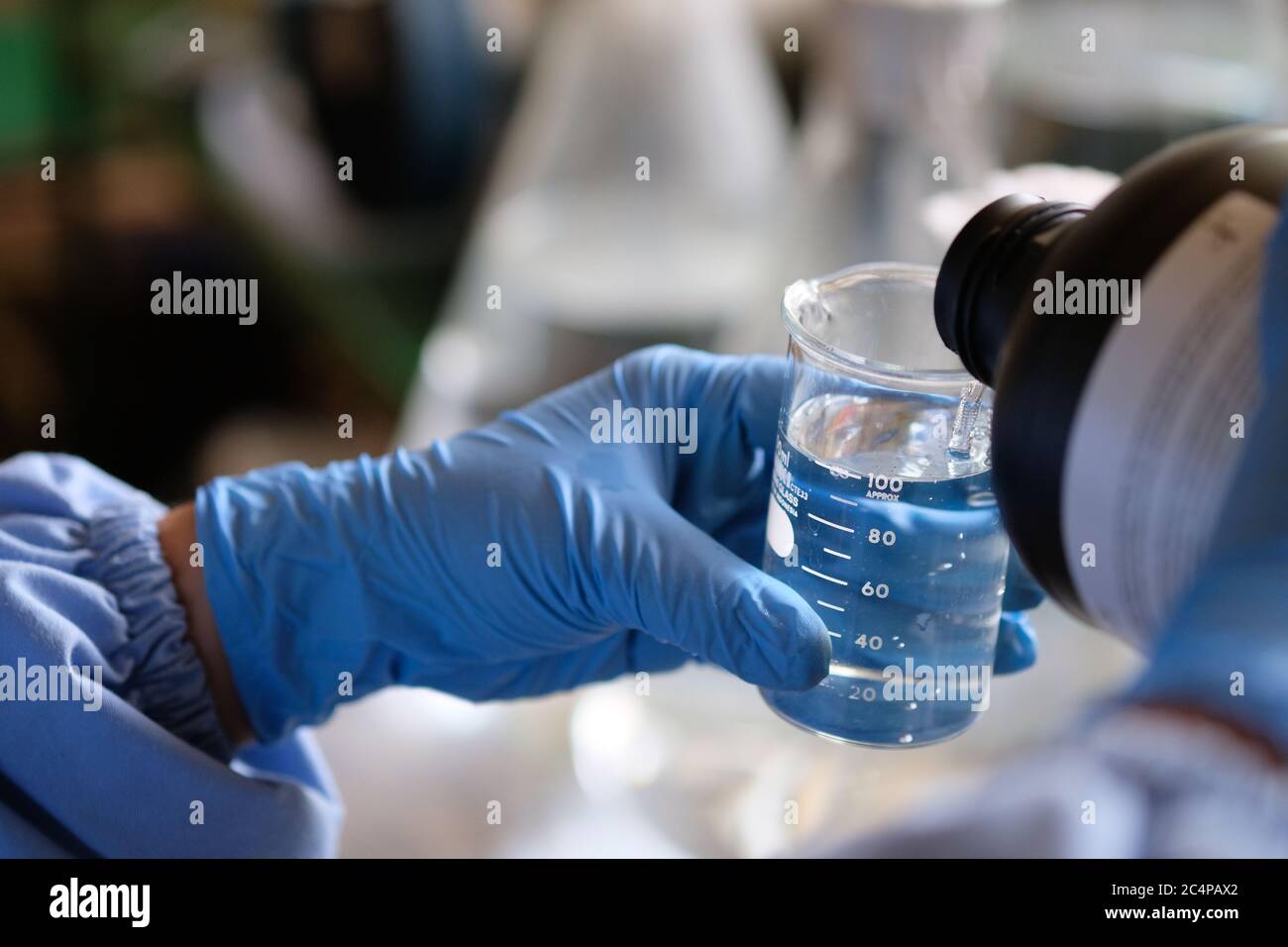 A researcher pouring chemical into beaker glass Stock Photo