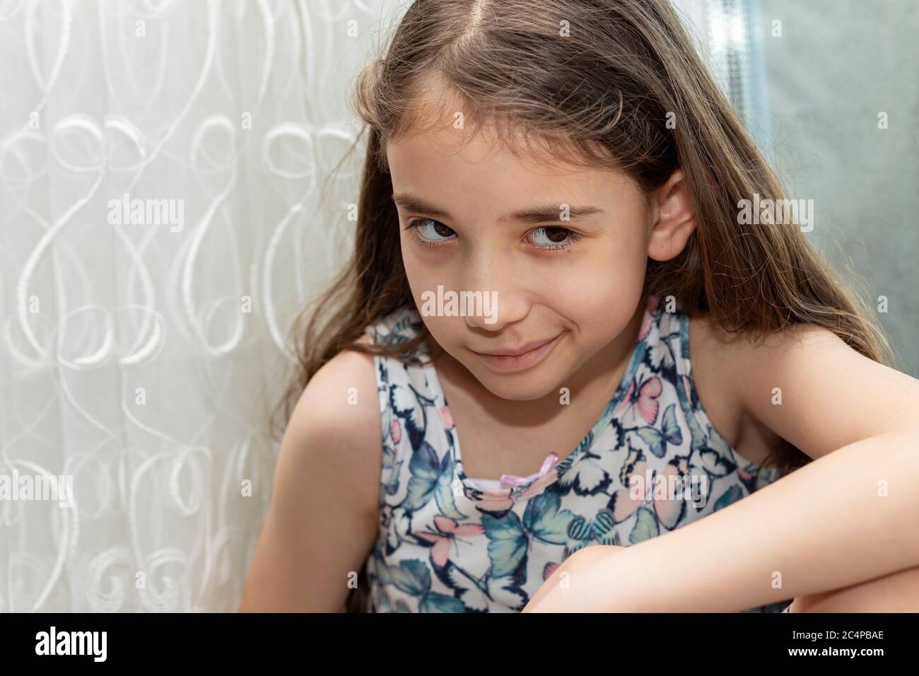 A little girl looking suspicious. The blonde girl with long hair takes a sceptical and suspicious-looking in front of the curtain. Stock Photo