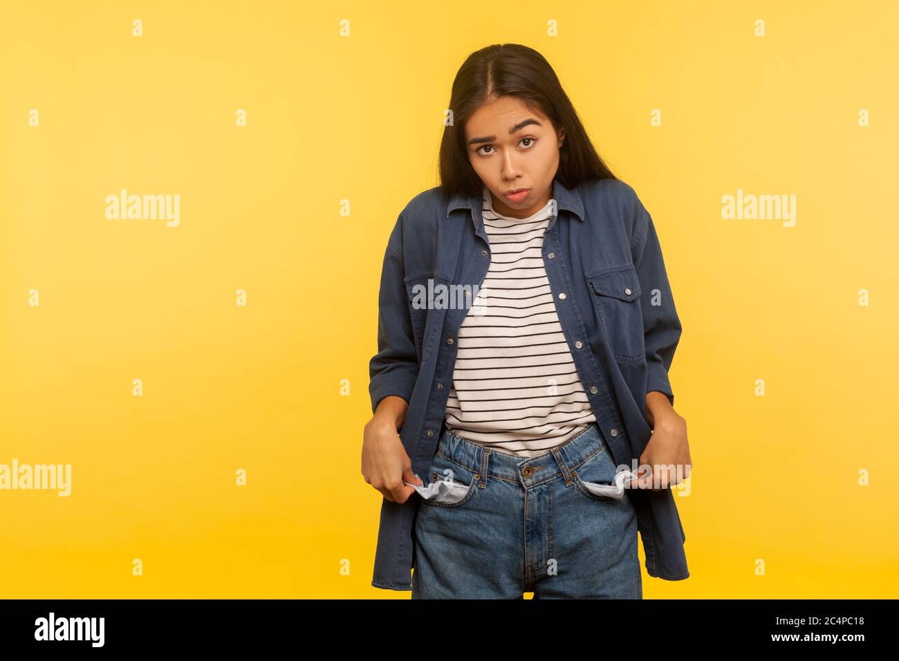 I'm bankrupt! Unhappy poor girl in jeans outfit turning empty pockets inside out and looking frustrated by overspend, lack of money, financial crisis. Stock Photo