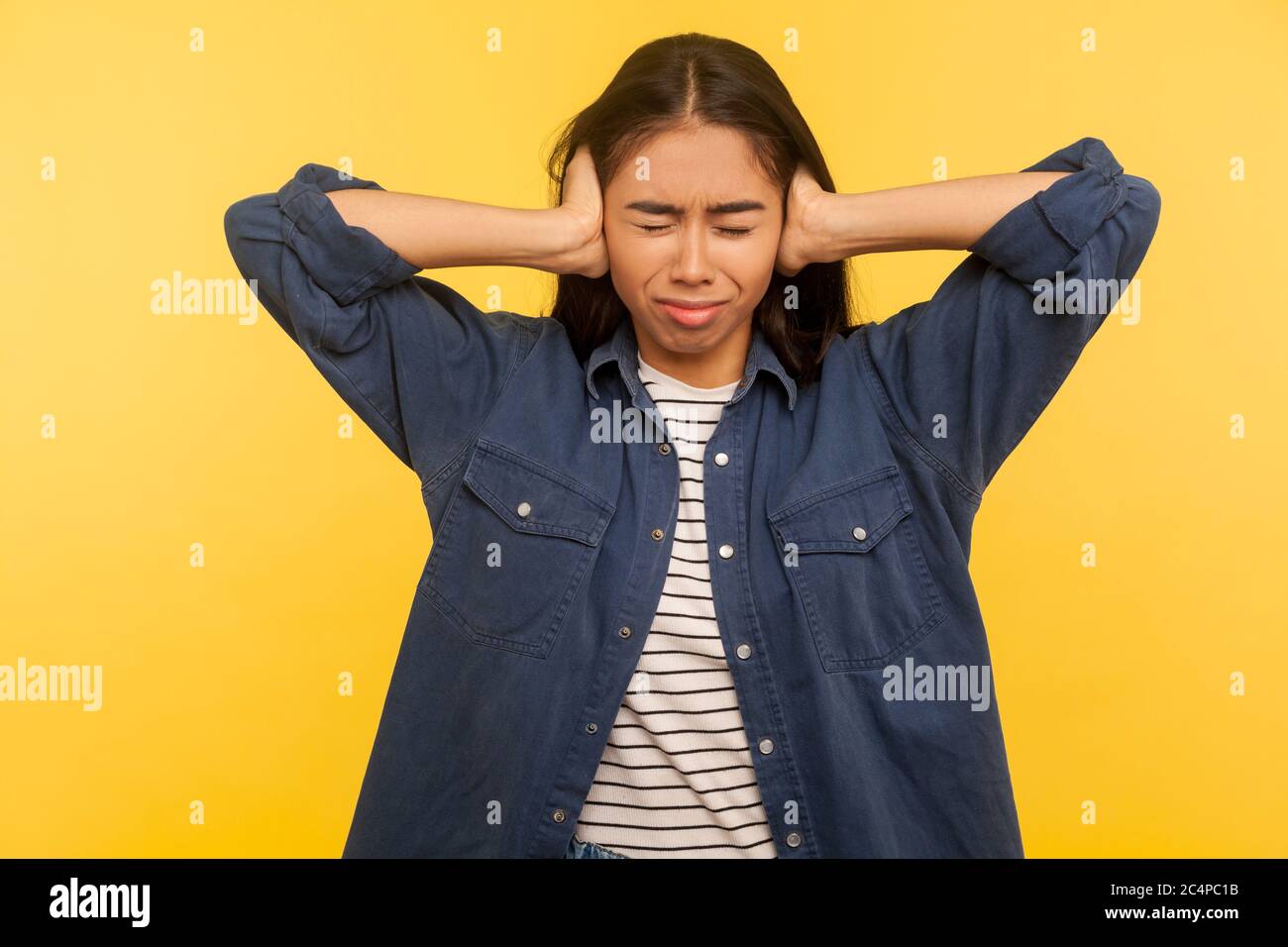 Don't want to hear! Portrait of irritated girl in denim shirt covering ears annoyed by unpleasant noise, loud voices, difficult to listen high sound. Stock Photo