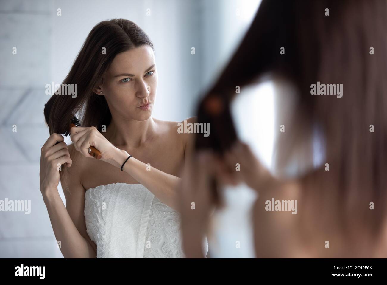 Unhappy woman brush tangled long hair in bathroom Stock Photo