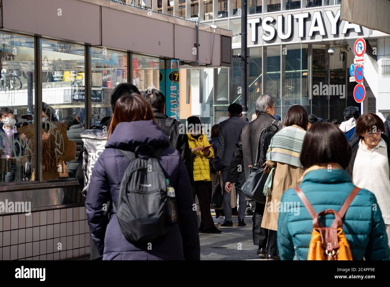 People walking on a sidewalk next to an exit/entrance of Metro station at Shibuya scramble crossing. Tsutaya building in the background. Tokyo, Japan. Stock Photo