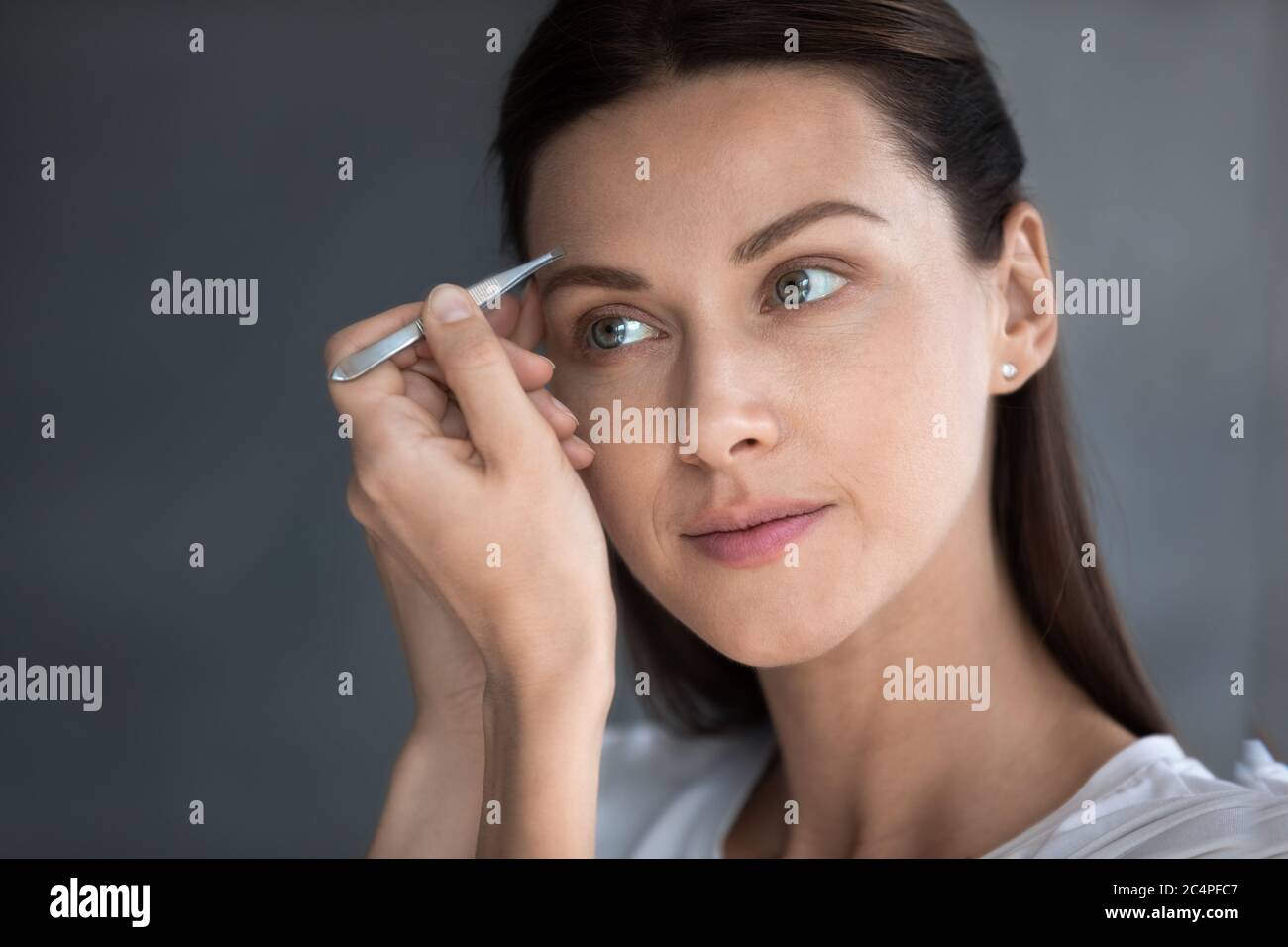 Young woman look in mirror pinch eyebrows with tweezers Stock Photo