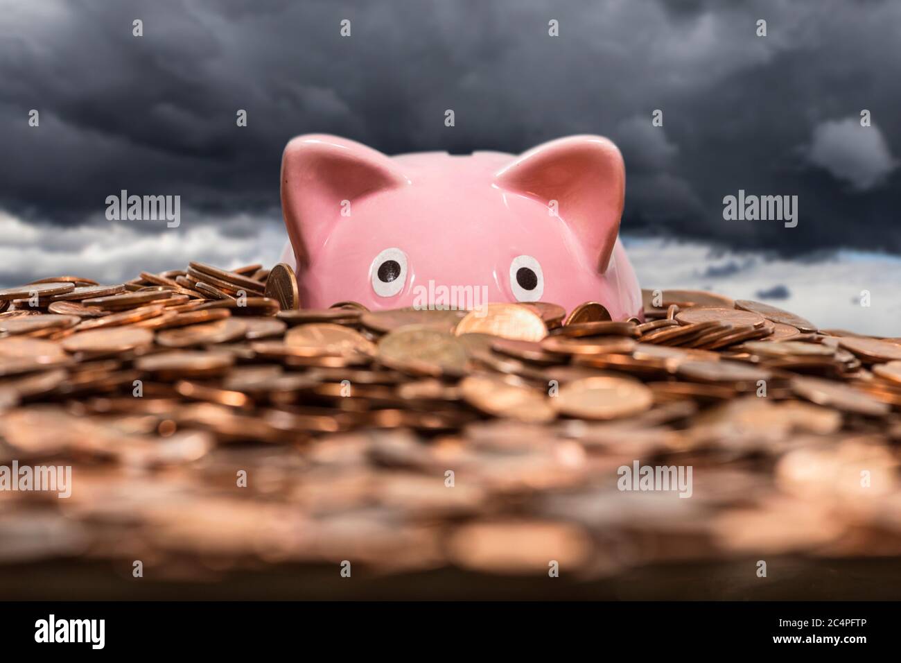 Pink piggy bank drowning in ocean of copper pennies with gathering storm clouds in background. Stock Photo