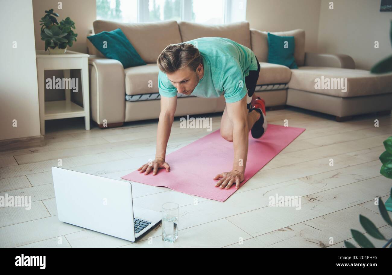 Blonde caucasian man with a laptop is doing fitness out from home on the floor Stock Photo