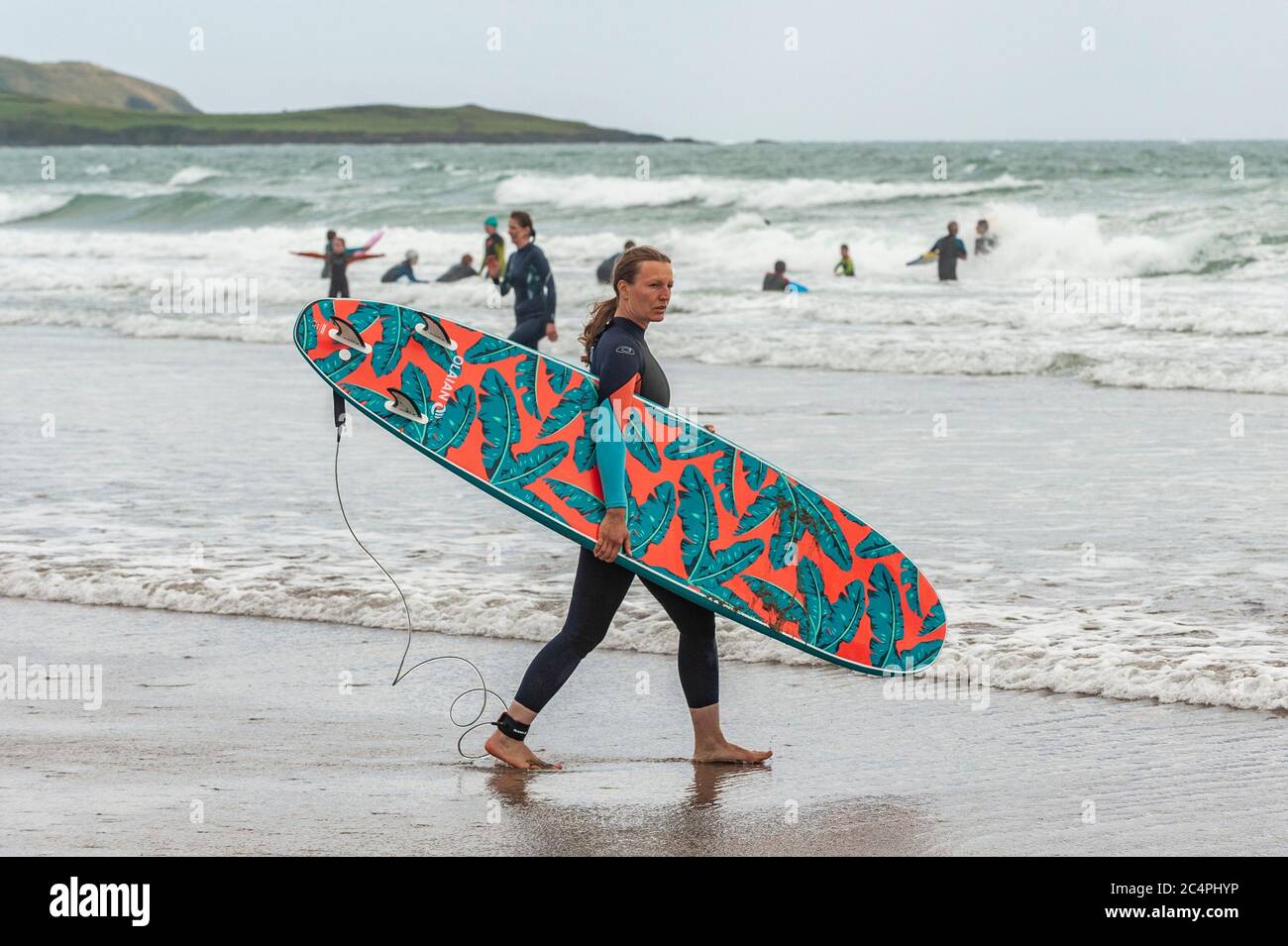 Garretstown, West Cork, Ireland. 28th June, 2020. On a very windy day at Garretstown Beach, a woman walks into the sea to surf some waves. Credit: AG News/Alamy Live News Stock Photo