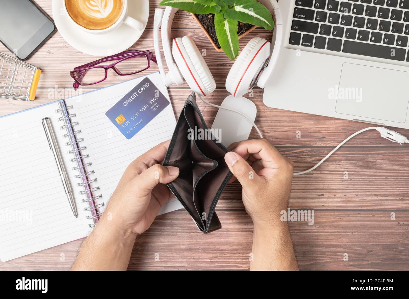 A man open wallet without money on the desk consisting of credit cards on notebook,  laptop computers with headphones and coffee, shopping online and Stock Photo