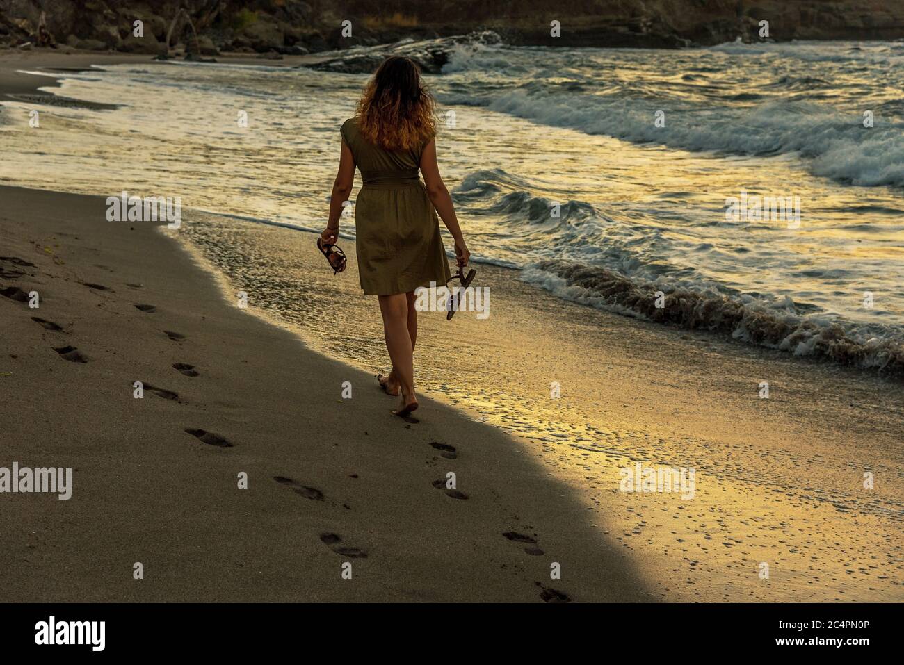 Woman walking on sandy beach in sunset leaving footprints in the sand ...