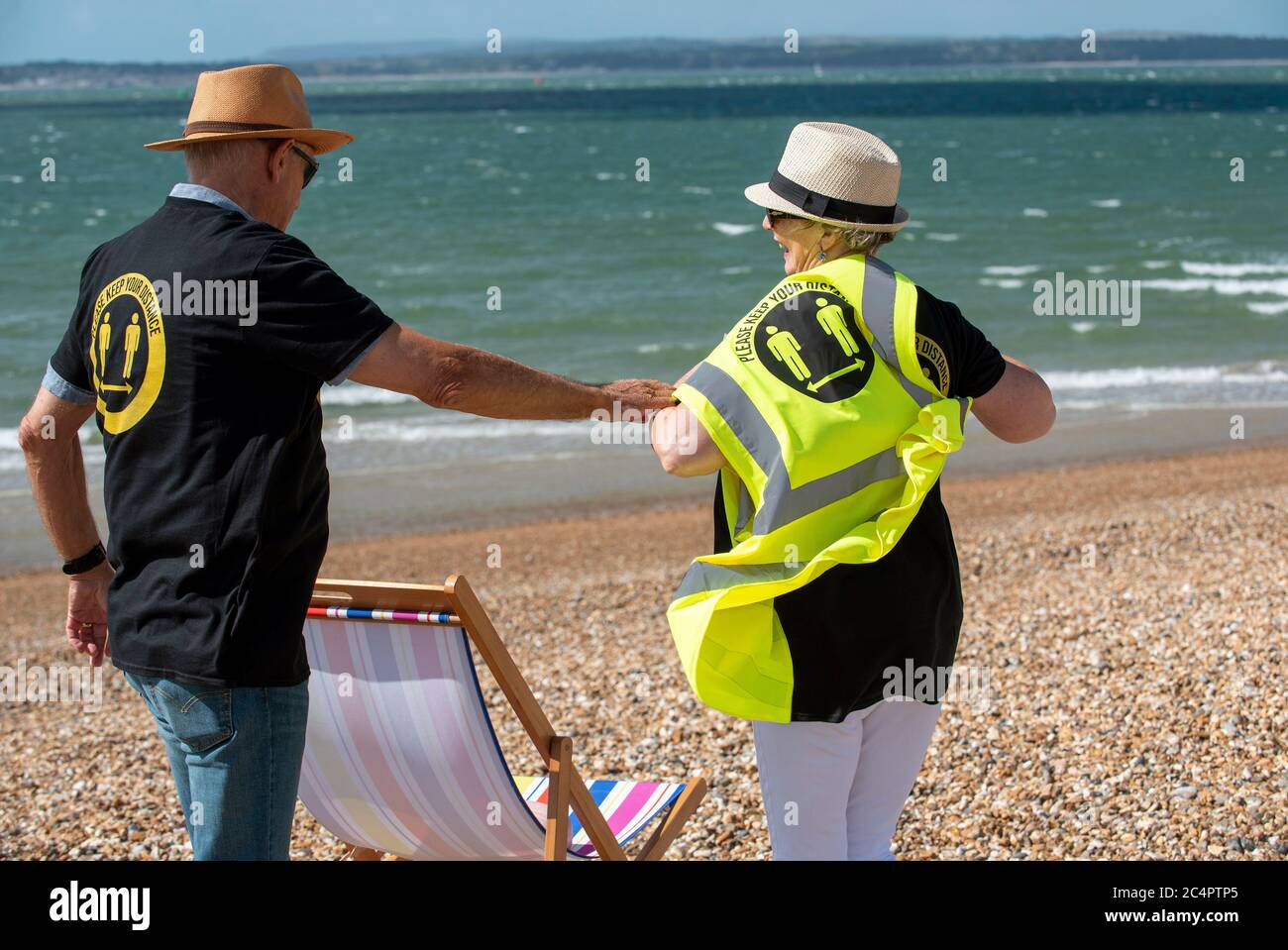 Southsea, Hampshire, England, UK. June 2020.  Man helping woman to  wear social distancing t shirt and keep your distance hi vis vest Stock Photo