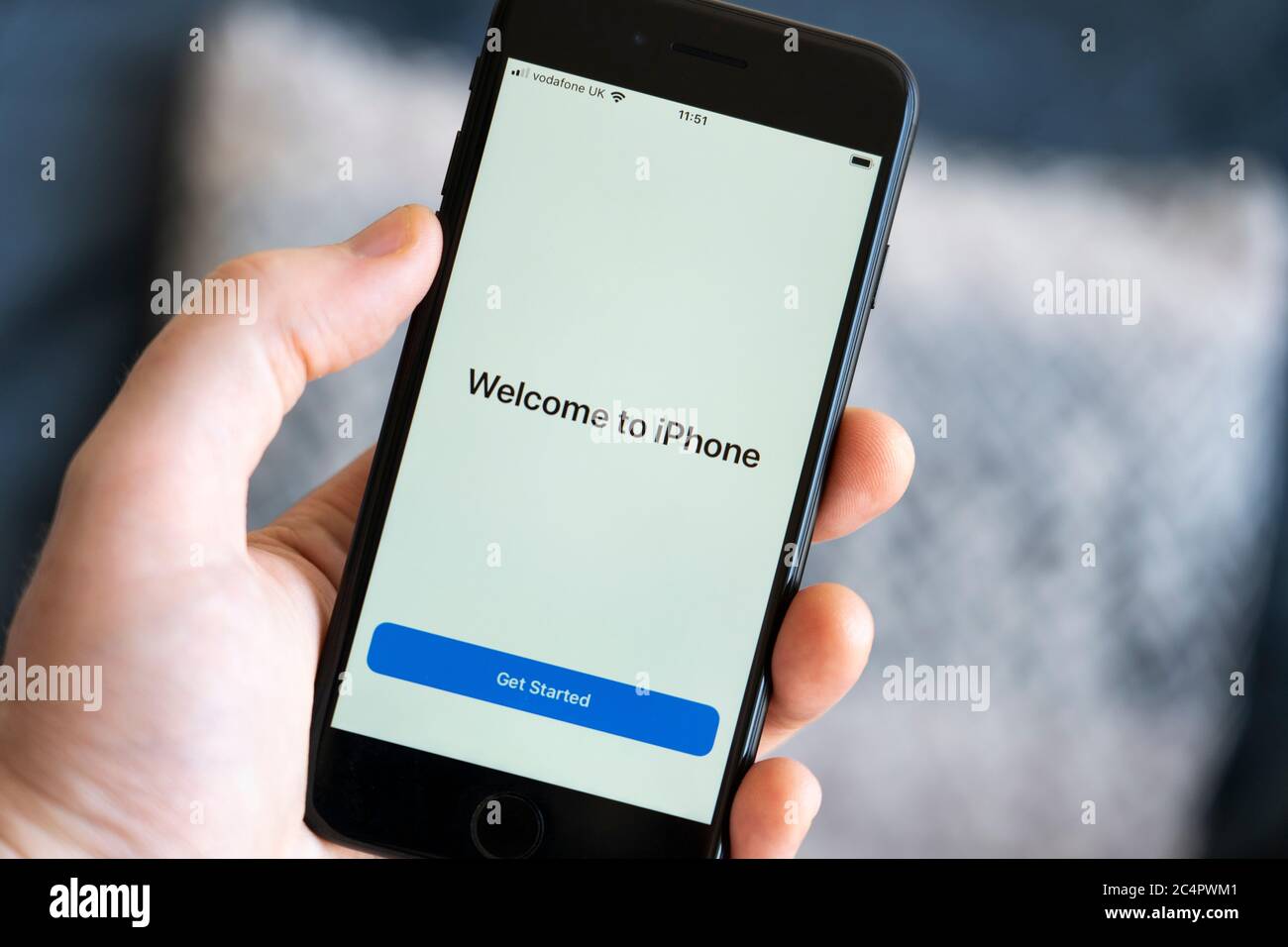 A man's hand holding an iPhone 7 cell phone showing a closeup of the start 'Welcome to iPhone' screen with a 'Get Started' introduction button, UK Stock Photo