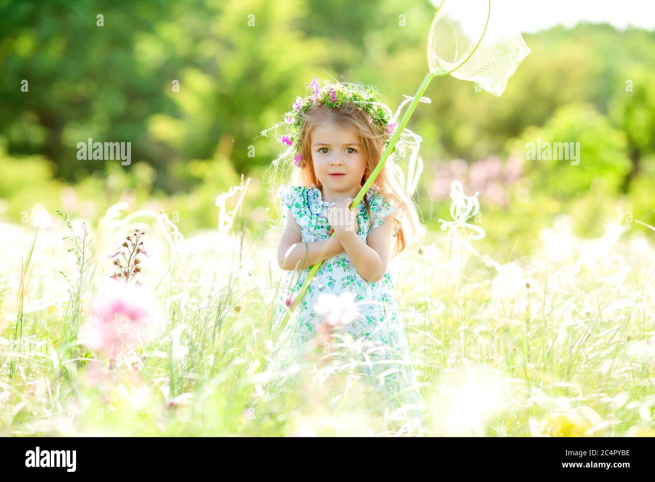 Cute little girl with a wreath on her head walks in a field and catches ...