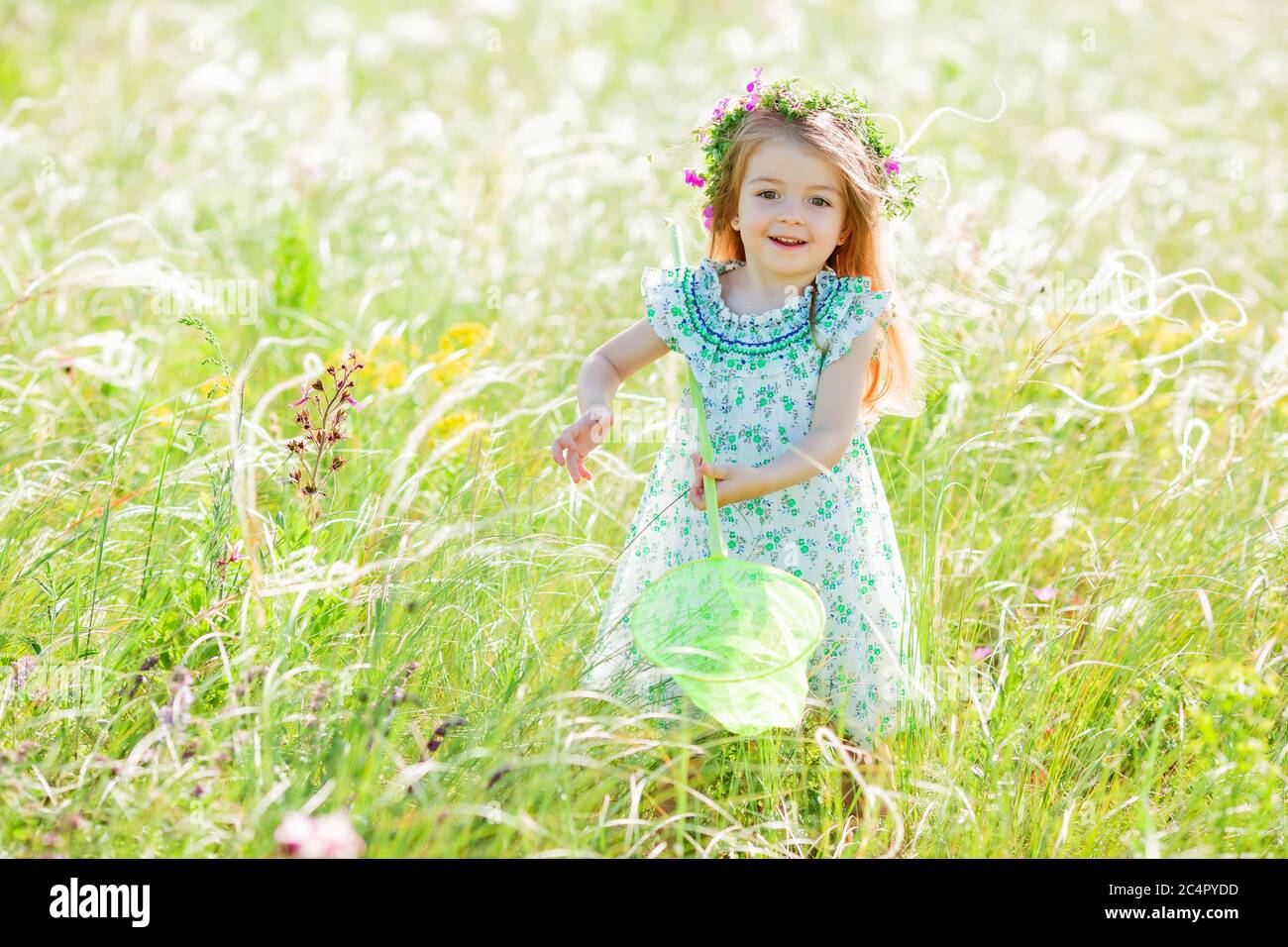 Cute little girl with a wreath on her head walks in a field and catches ...