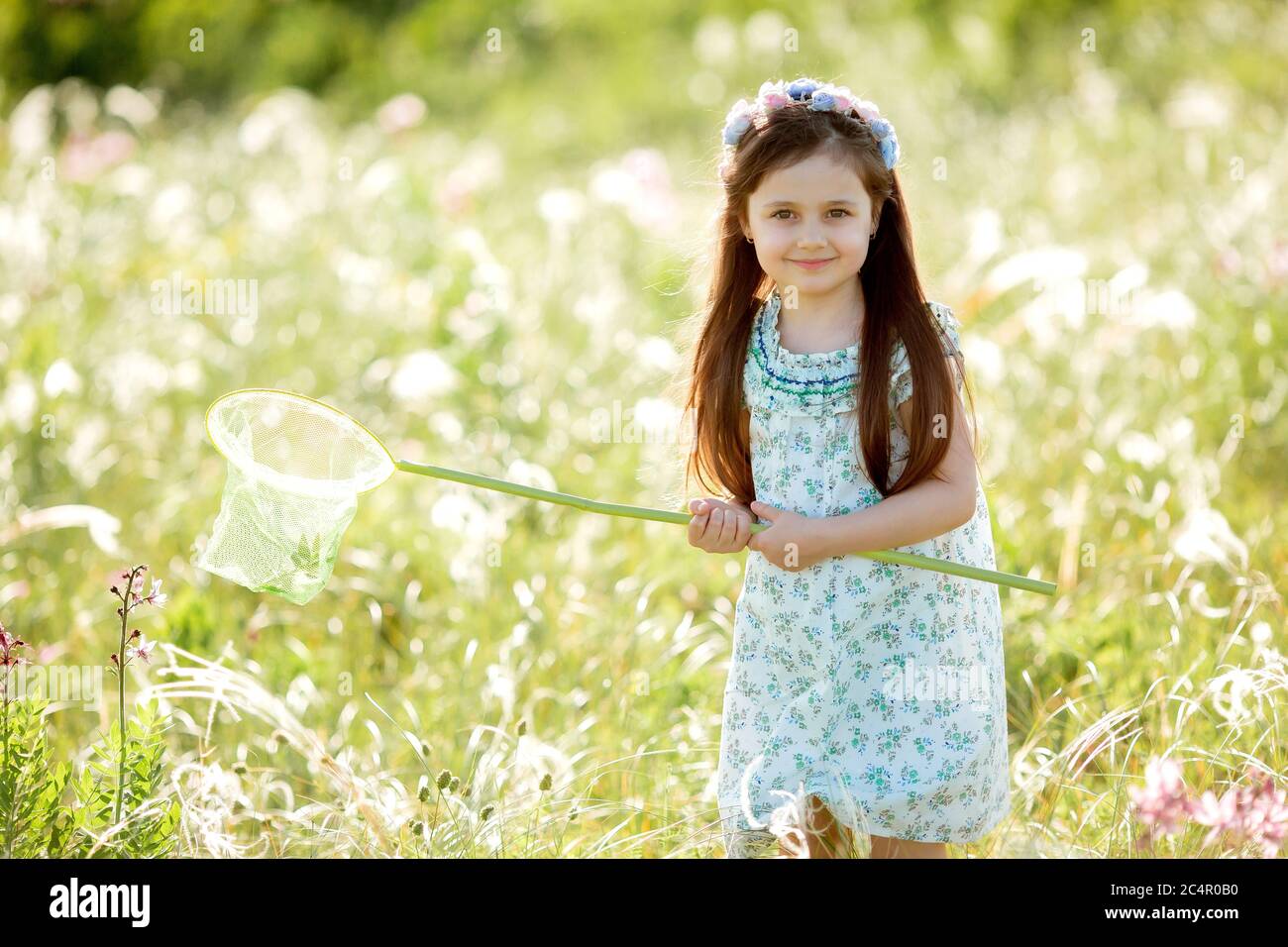 Cute little girl with a wreath on her head walks in a field and catches ...