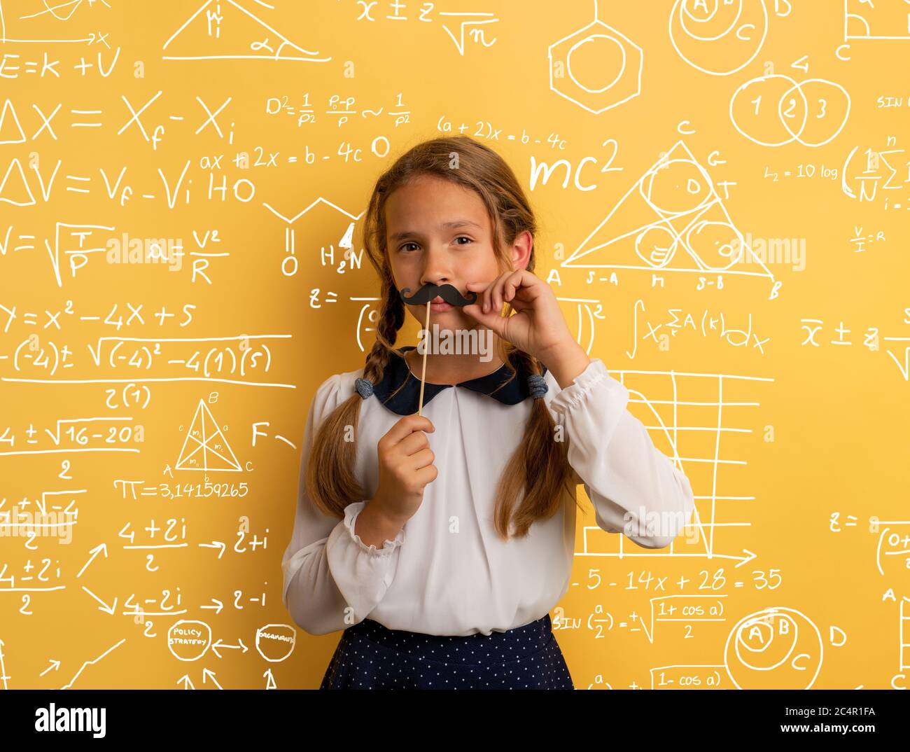 Young student acts like a senior teacher and wants to solve an advance math problem. Yellow studio background Stock Photo