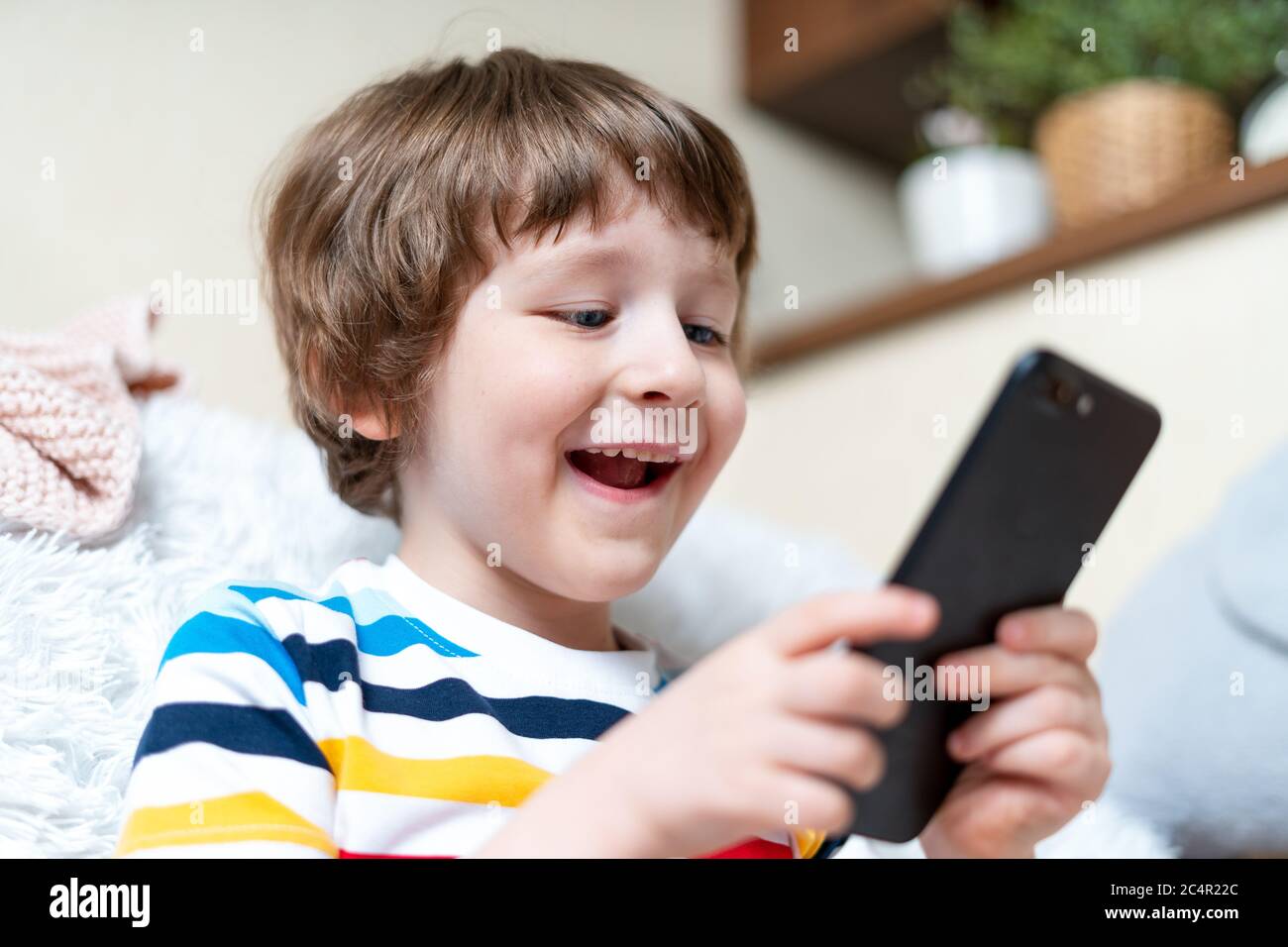Happy little child boy playing online game, watching video on cellphone, sitting on couch entertaining in living room. Smiling small kid using funny m Stock Photo - Alamy Happy little child boy playing online game, watching video on cellphone, sitting on couch entertaining in living room. Smiling small kid using funny m Stock Photo - Alamy