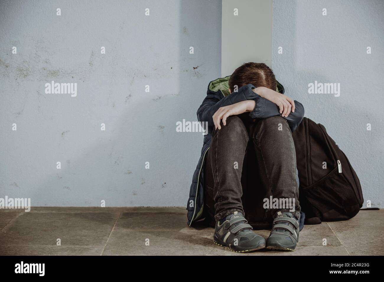 Little boy or school child sitting alone on floor in front of the school after suffering an act of bullying Stock Photo