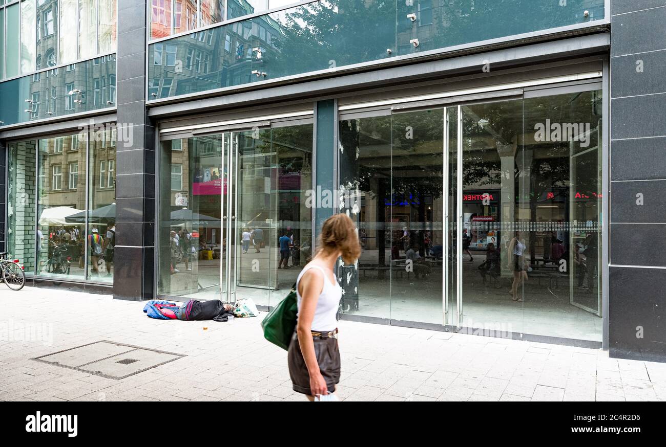 Hamburg, Germany. 27th June, 2020. A woman walks past an empty shop in Spitalerstrasse, in front of which a man is lying in a sleeping bag. Credit: Markus Scholz/dpa/Alamy Live News Stock Photo
