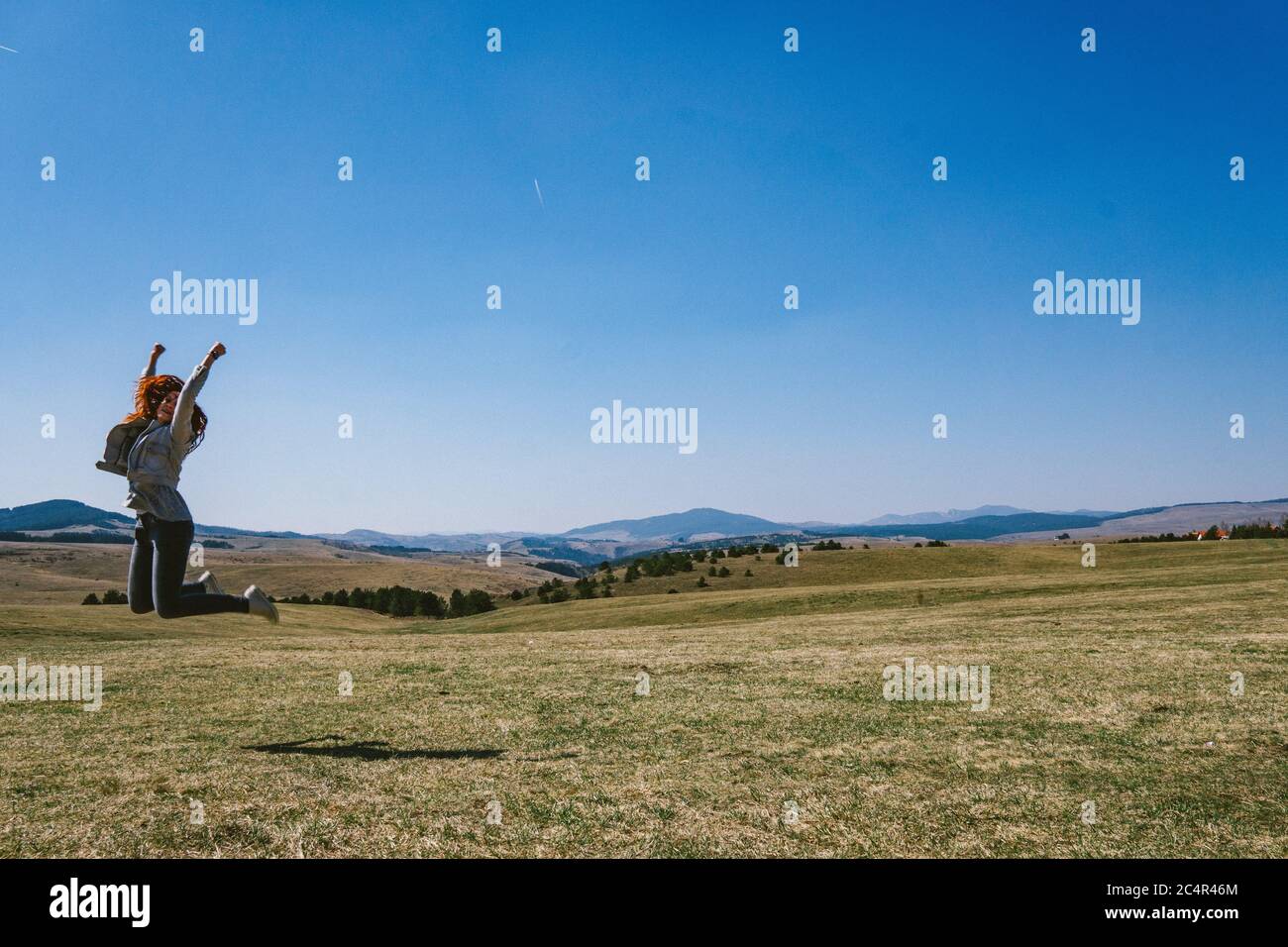Woman jumping on a field at mountain Stock Photo