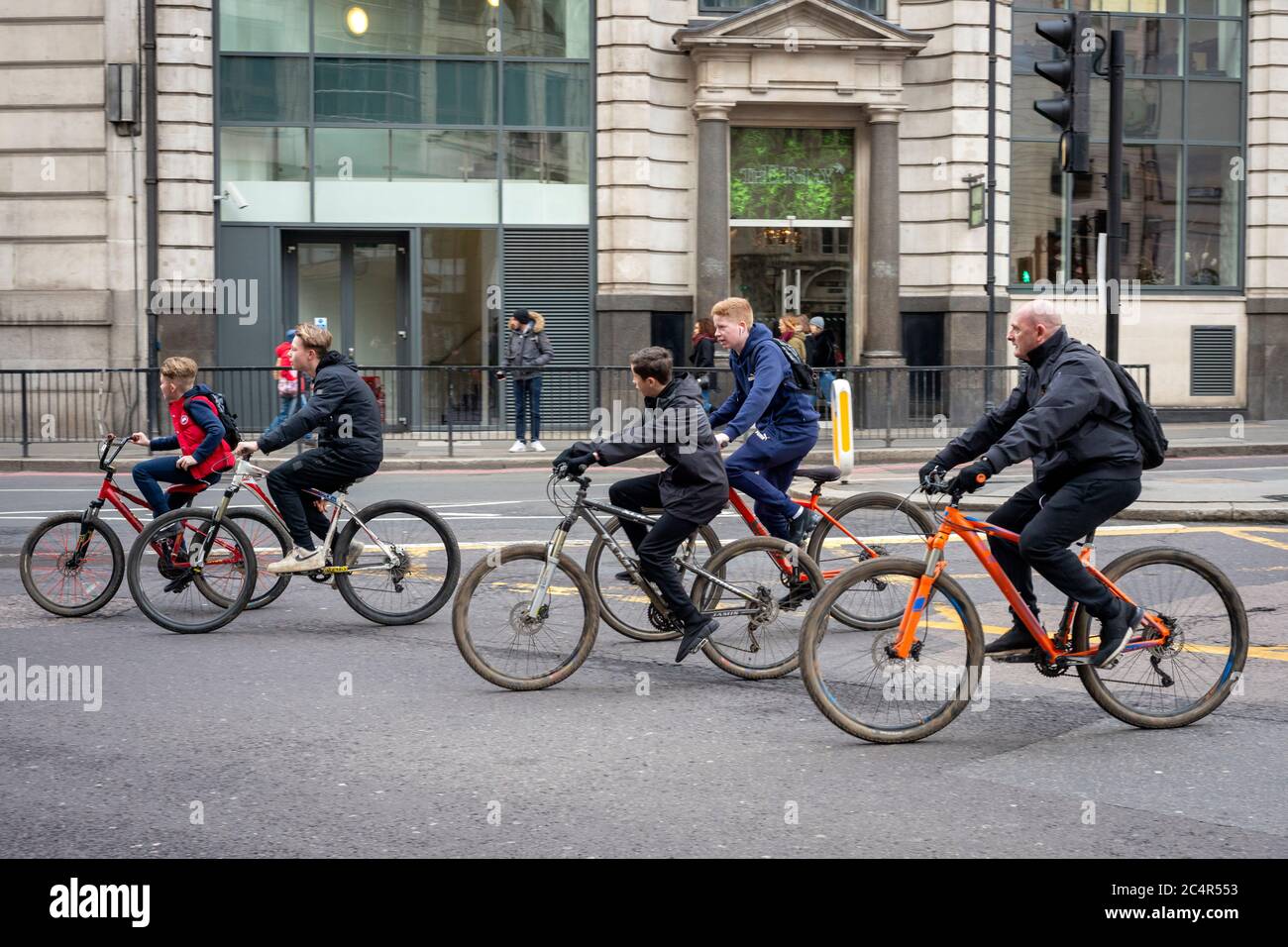 Street view of group of teenagers and one adult cycling casual careless and unprotected with no helmets on King William Street in the London City on Sunday morning, London, UK Stock Photo