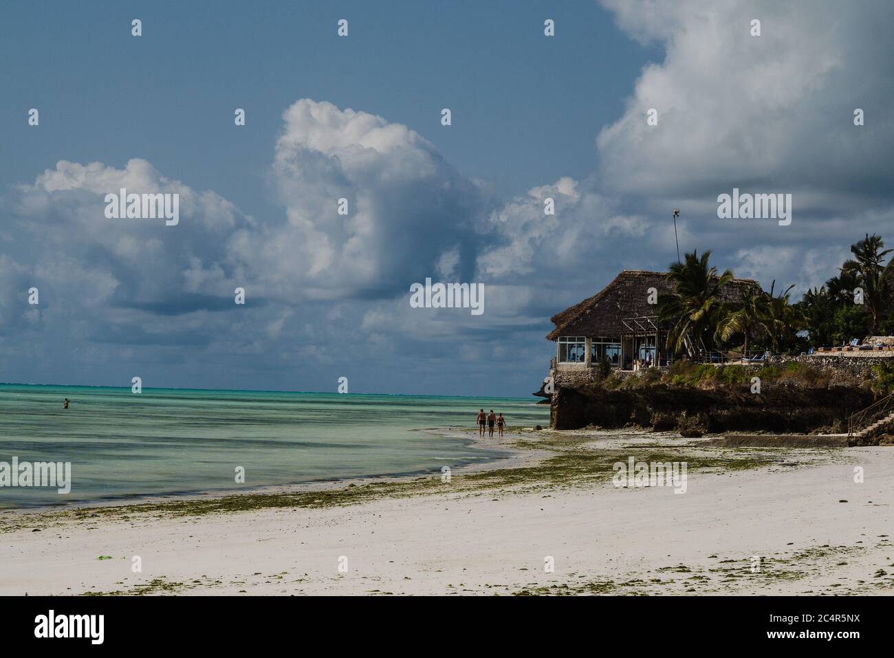 Tourists walking along Jambiani beach with a beachfront hotel nearby, in Zanzibar, Tanzania Stock Photo