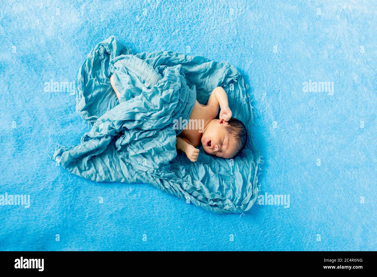 Newborn 14 day old baby boy lying on his back crying on blue wrap cloth ...