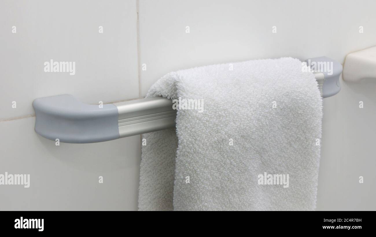 White towel hanging on a aluminum towel holder with a wall of white ceramic background Stock Photo