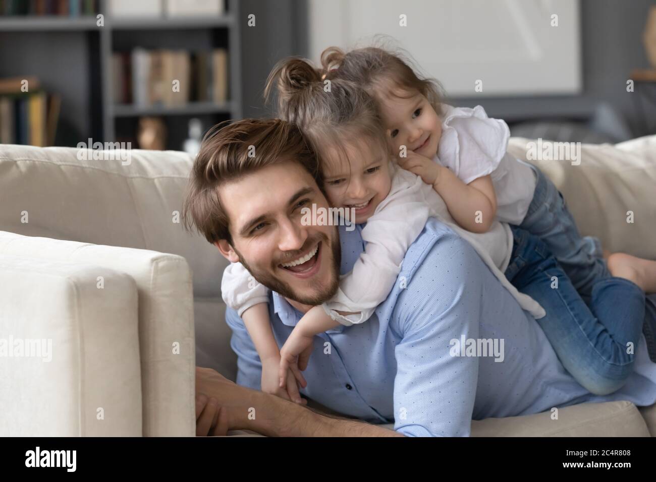 Two cute little girls lying on smiling father back Stock Photo
