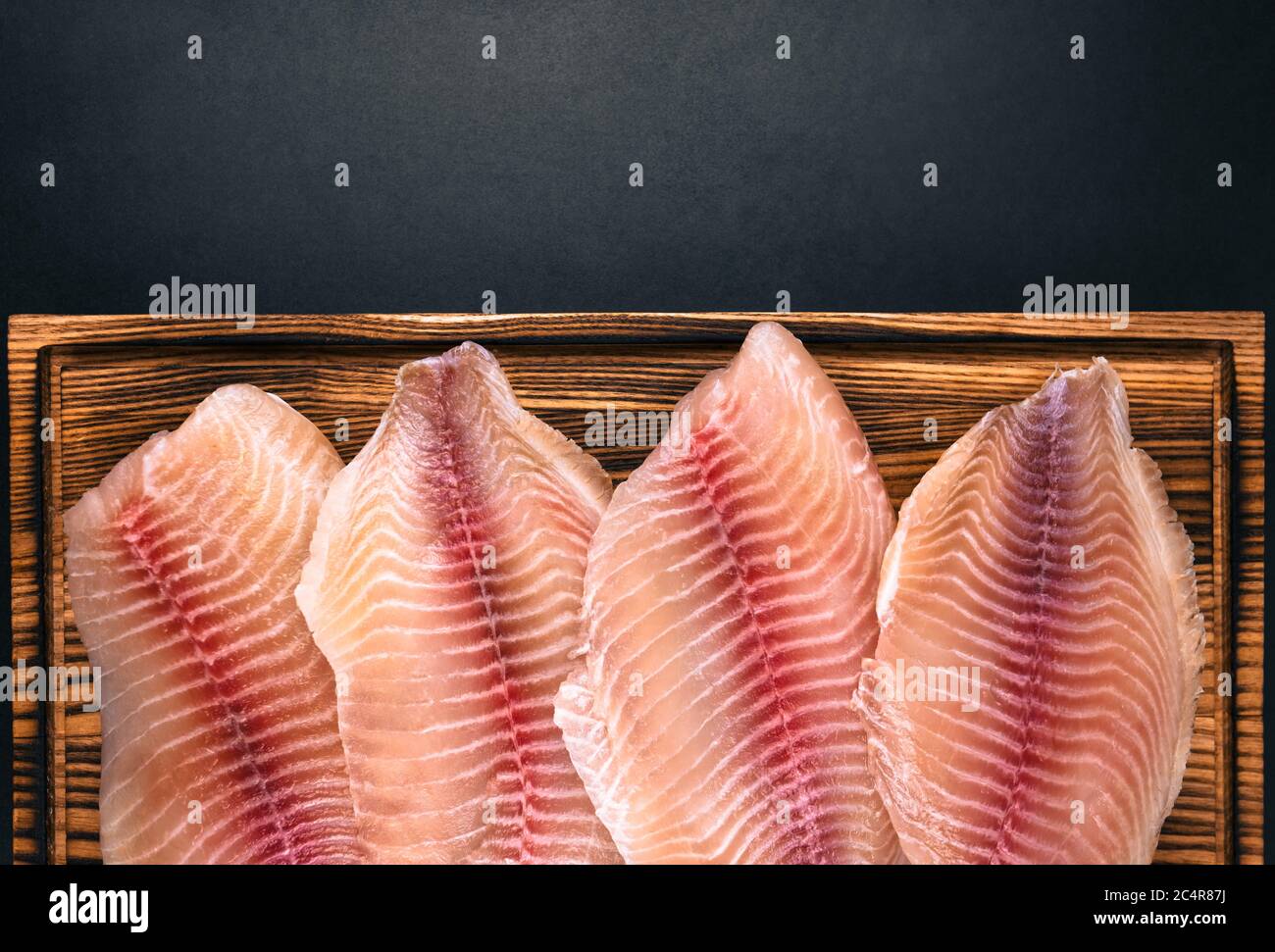 Fresh fillet of white tilapia fish laid a wooden board. Stock Photo