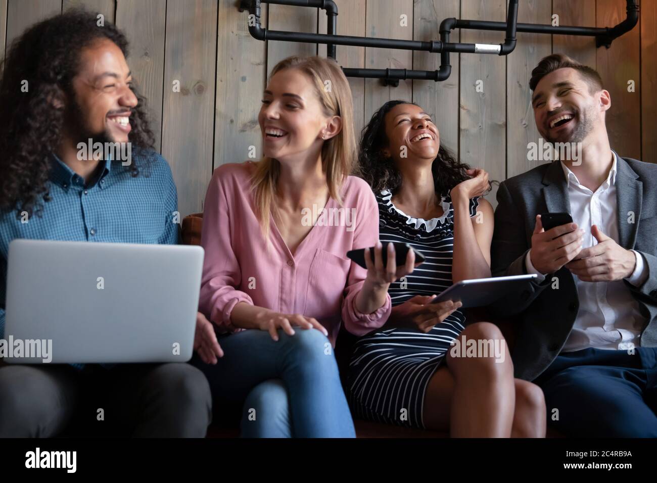 Multiethnic friends holding gadgets laughing over funny videos Stock Photo
