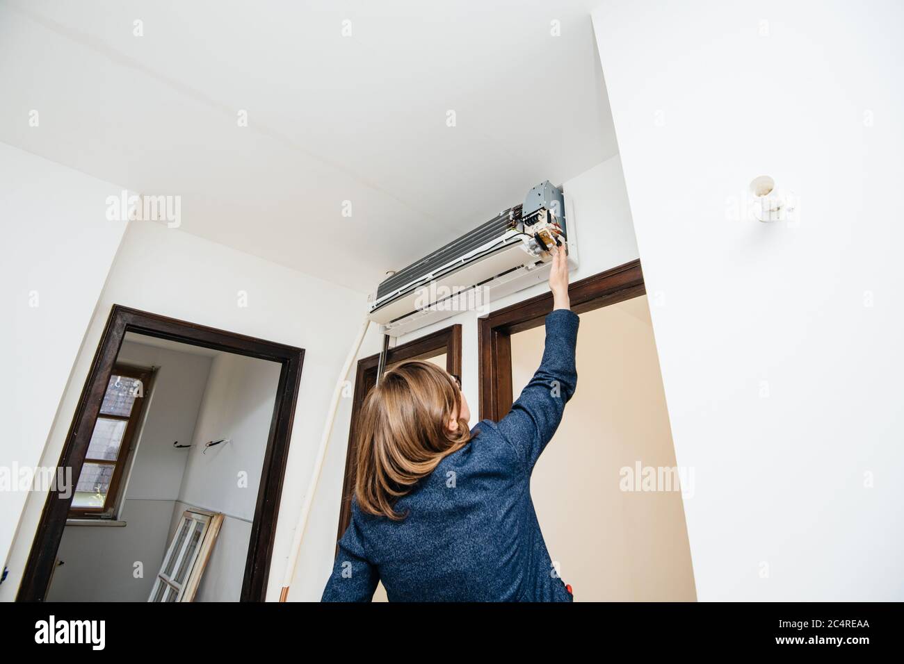 Rear view of engineer woman testing measuring trying to repair newly installed air conditioner wall ac unit Stock Photo