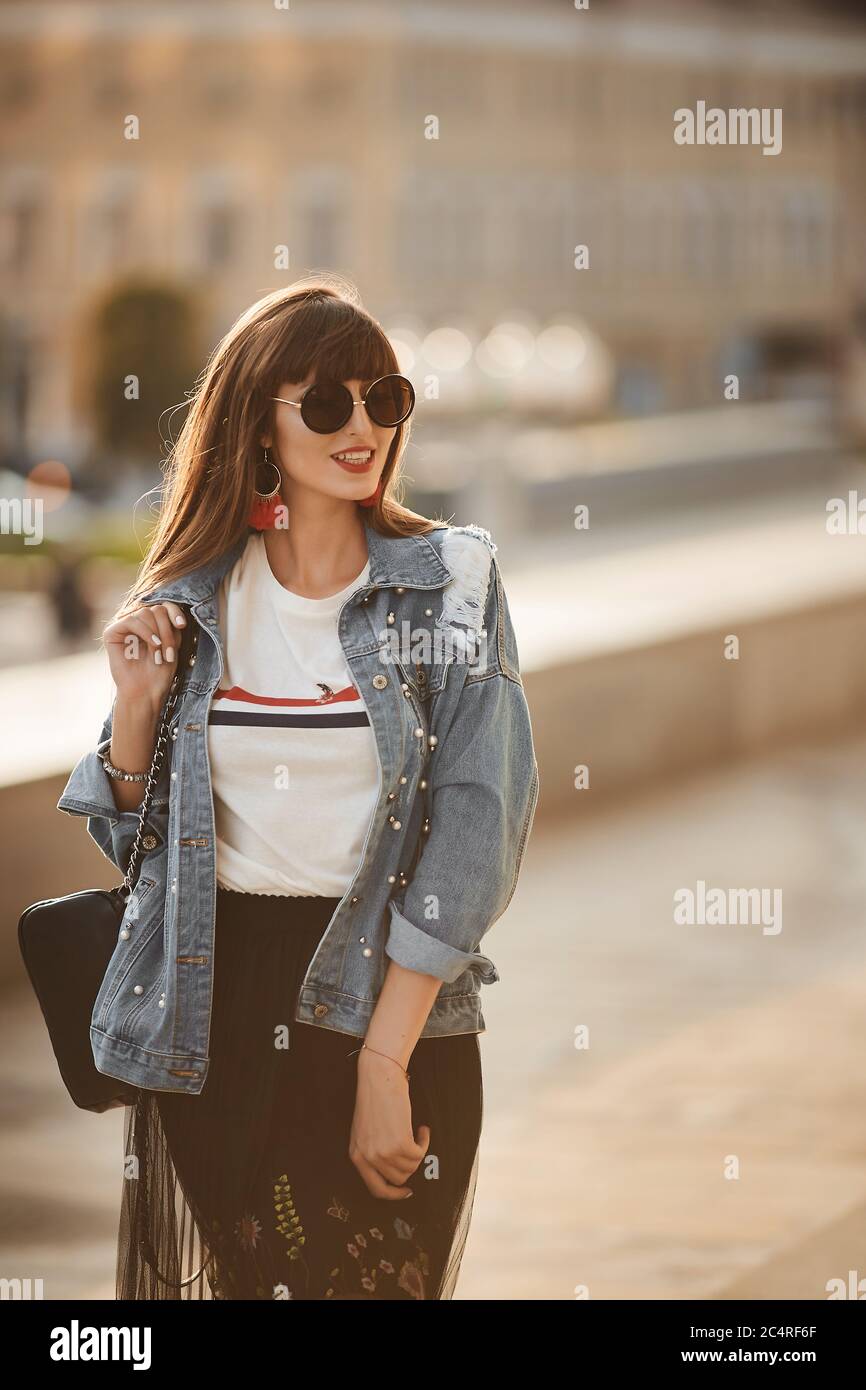 Young hipster girl in a denim jacket and round sunglasses walking at the city street in the summer day Stock Photo Alamy