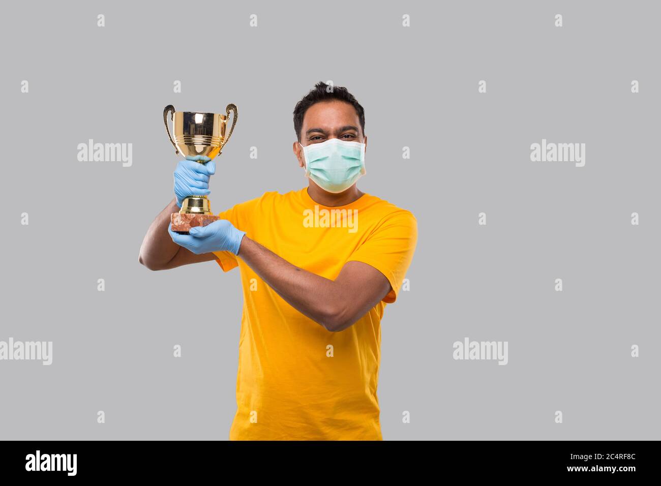 Indian Man Holding Trophy in Hands WEaring Medical Mask and Gloves Isolated Stock Photo