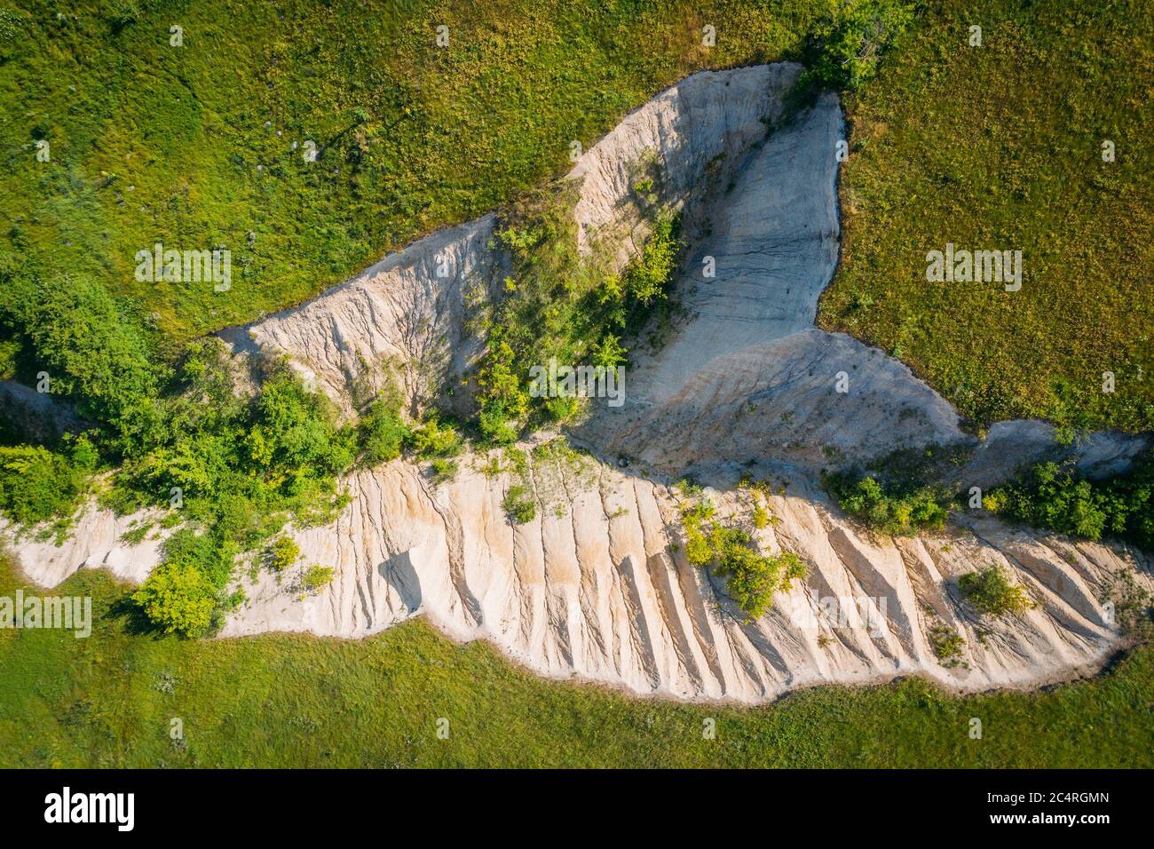 Chalk crevice or ravine among green grass meadow hills, aerial top view, abstract nature background. Stock Photo