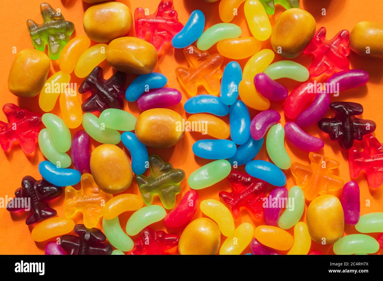 Multi-colored glazed jelly beans sweets on orange paper background. Stock Photo