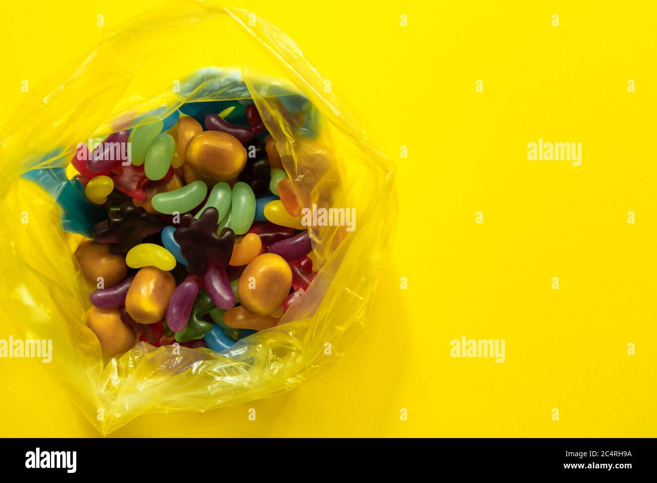 Multi-colored glazed jelly beans sweets in plastic package on yellow paper background. Stock Photo