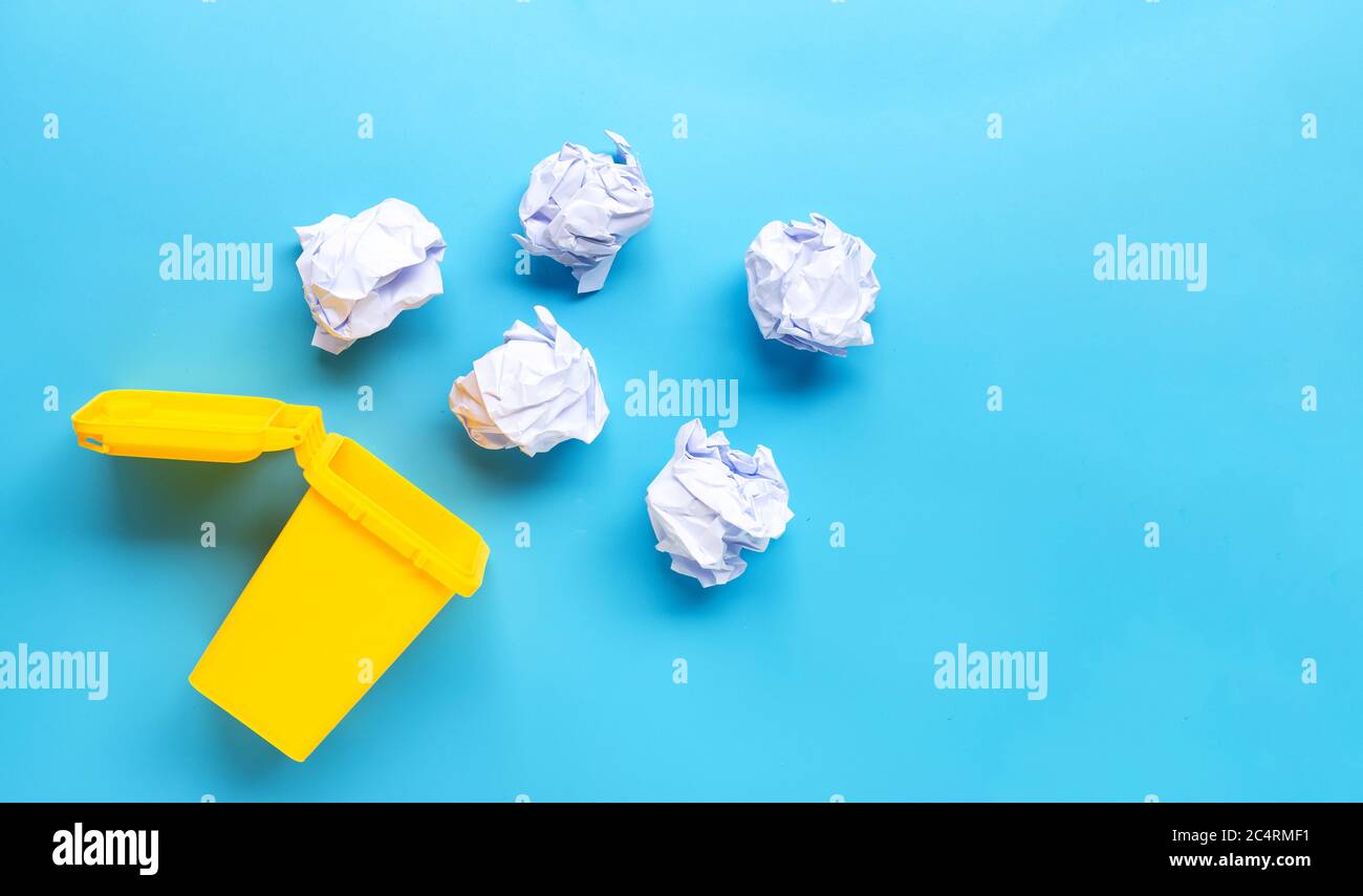 Yellow bin with white crumpled paper on blue background. Top view Stock