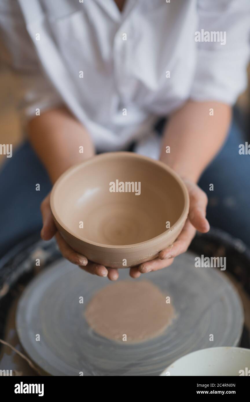 The female potter finished making a clay vase remove it from the potter's wheel. Creating vase of white clay. Making ceramic products from white clay Stock Photo