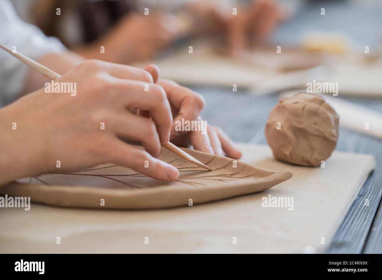 Female potters hand making clay pottery at the table with a different wooden tools close up. Stock Photo