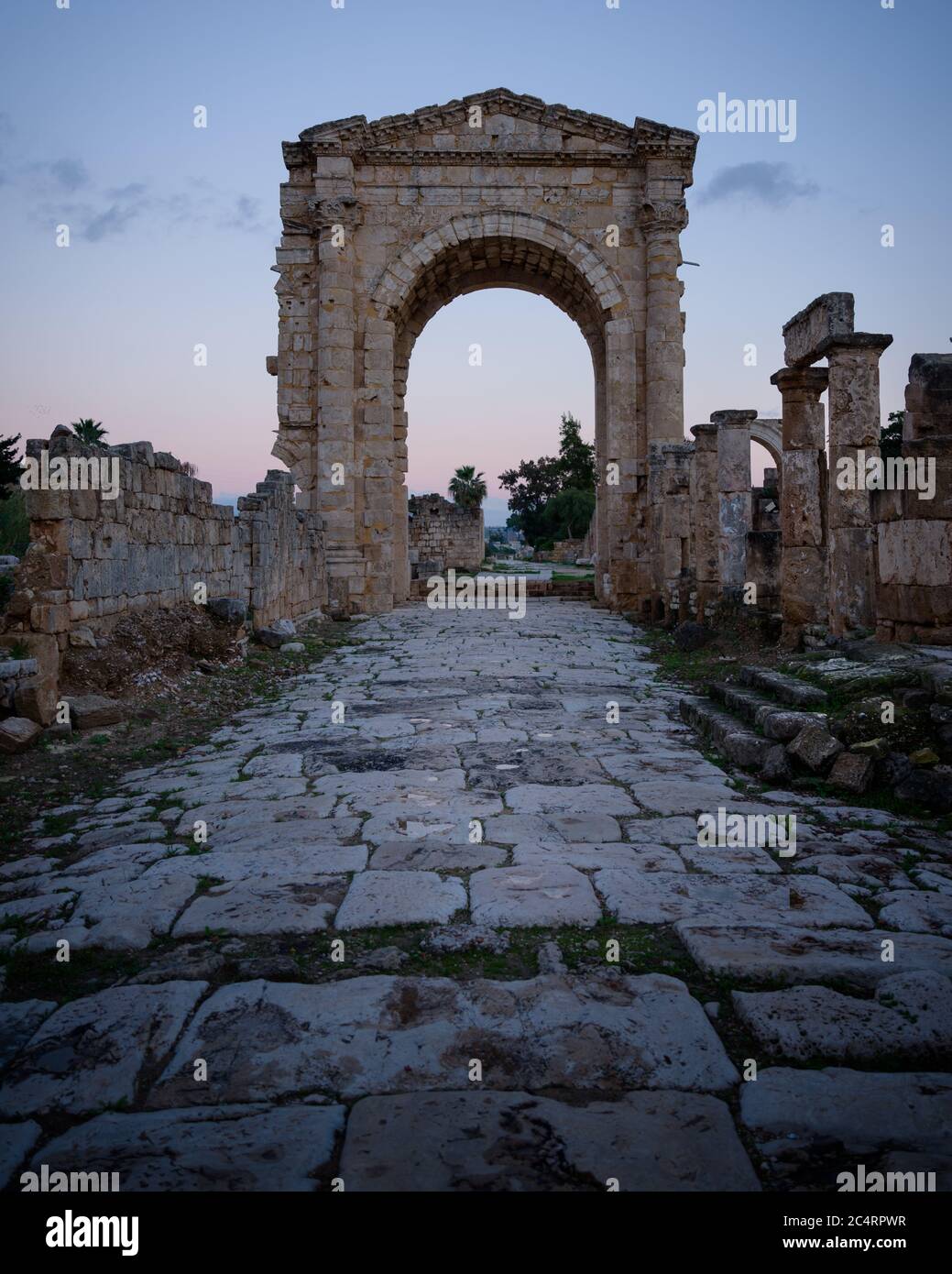 Monumental triumphal arch gate in Tyre Roman hippodrome, with ancient paving stone way leading through ruined columns and buildings, Lebanon, Middle E Stock Photo
