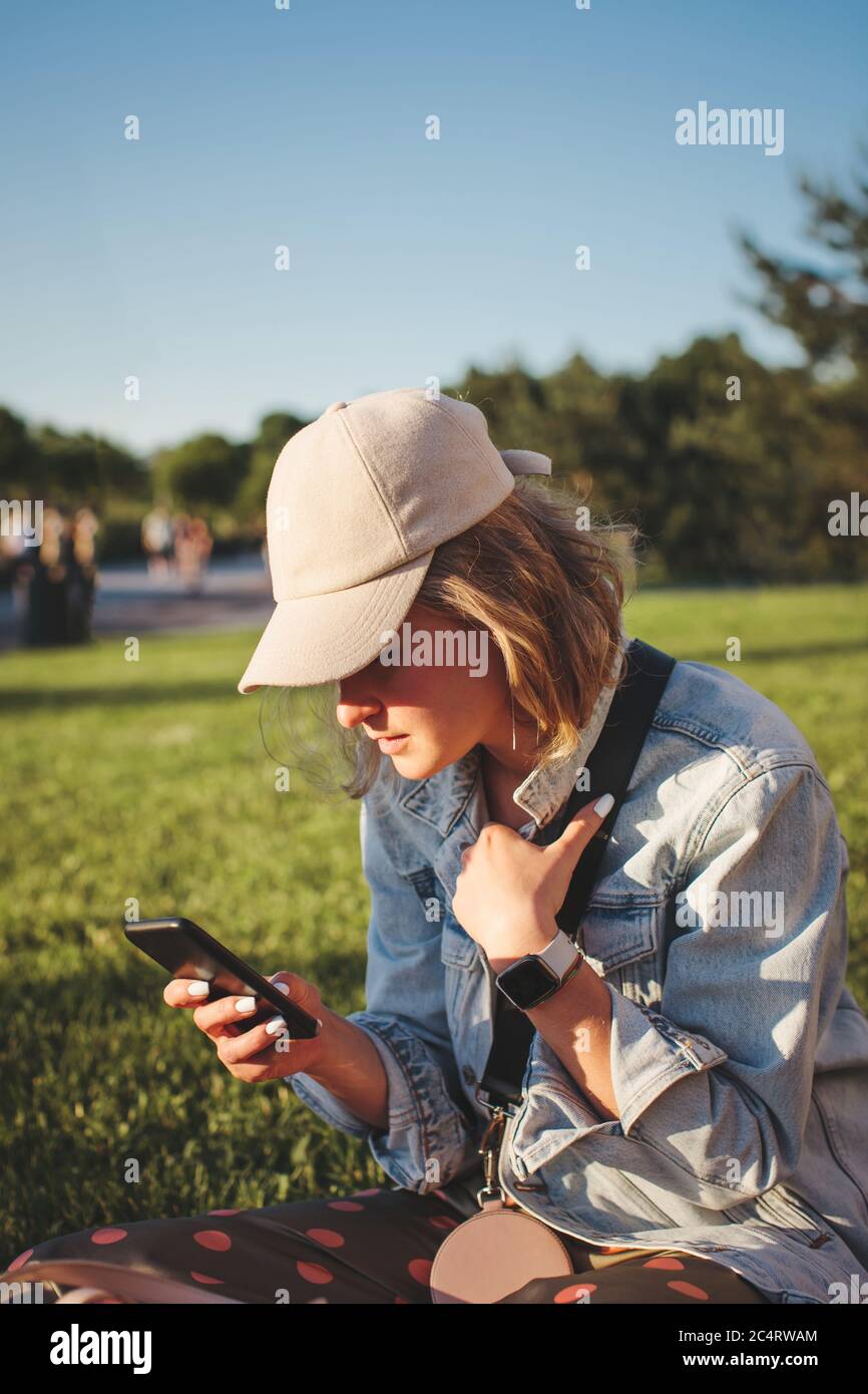 Beautiful blonde girl in a cap with short hair sits in a group of girls and looking away. Selective focus. Stock Photo