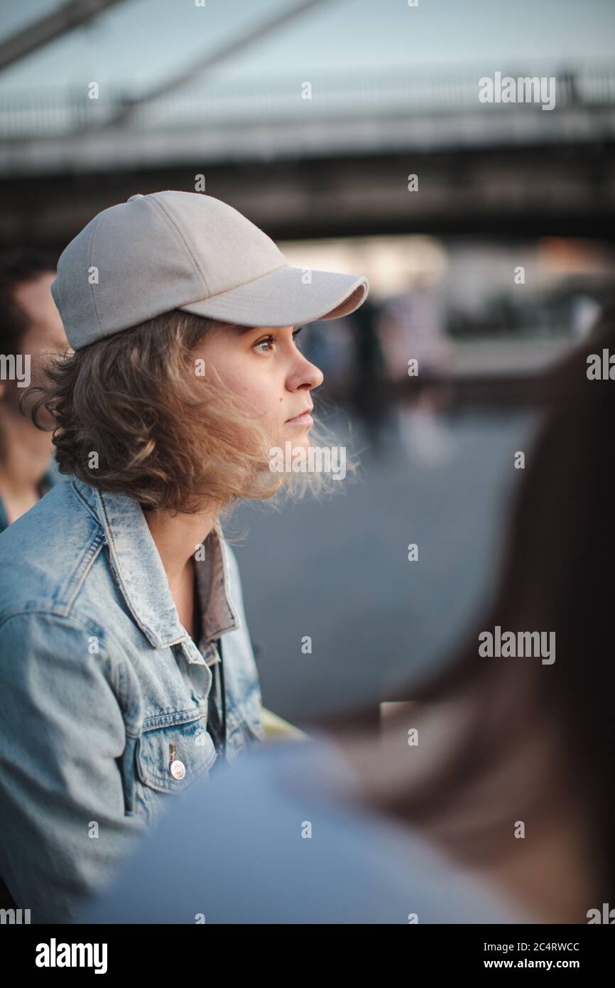 Beautiful blonde girl in a cap with short hair sits in a group of girls and  looking away. Loneliness among friends. Selective focus Stock Photo - Alamy