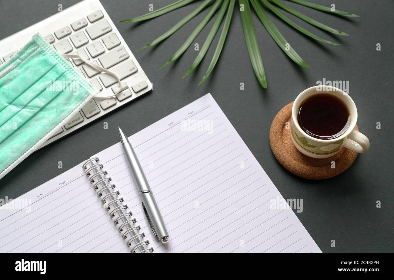 Top view of office desk with computer keyboard, medical face mask, notepad, coffee and green plant. Stock Photo