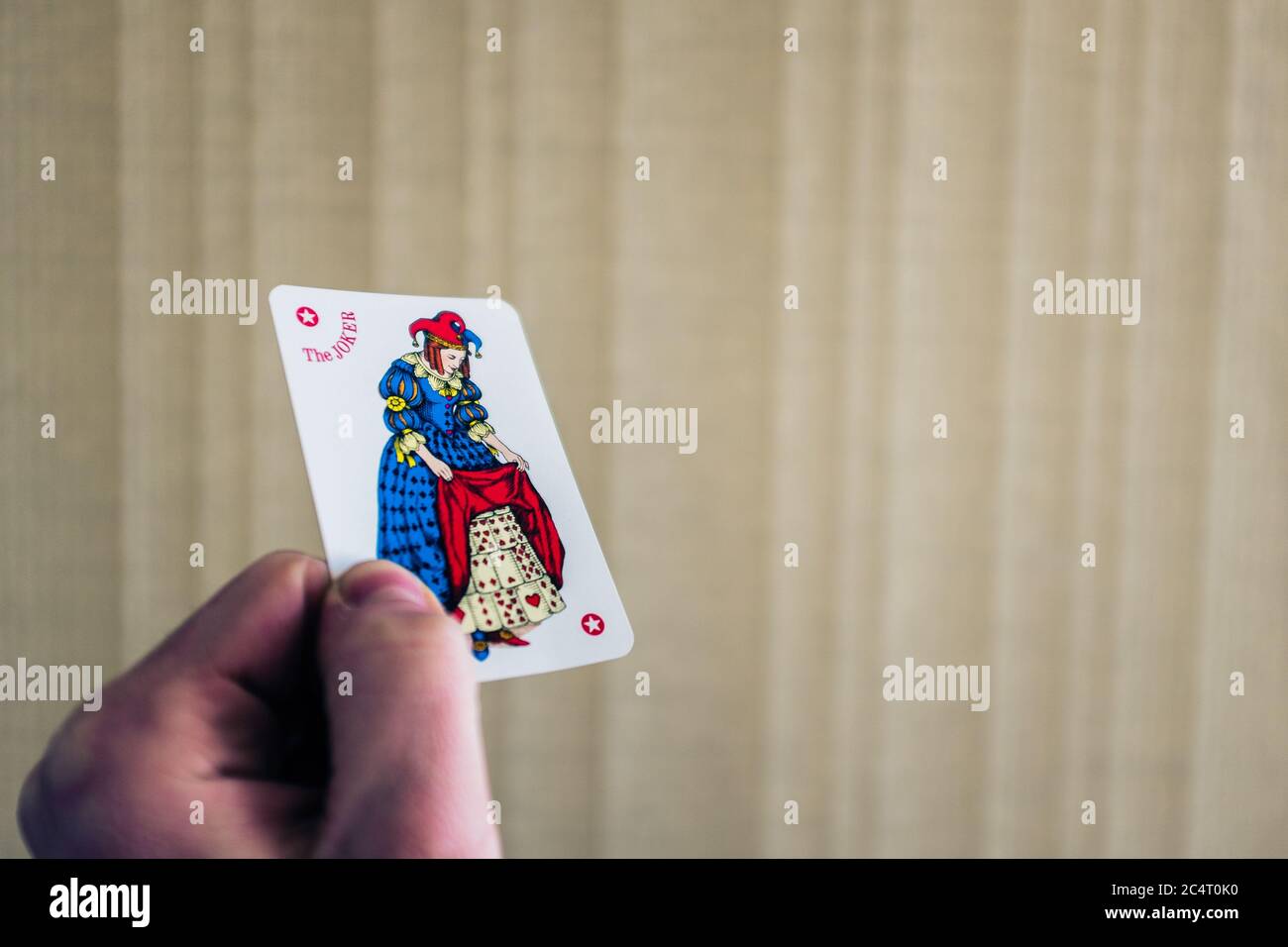 Closeup shot of a person holding the joker card behind a light background Stock Photo