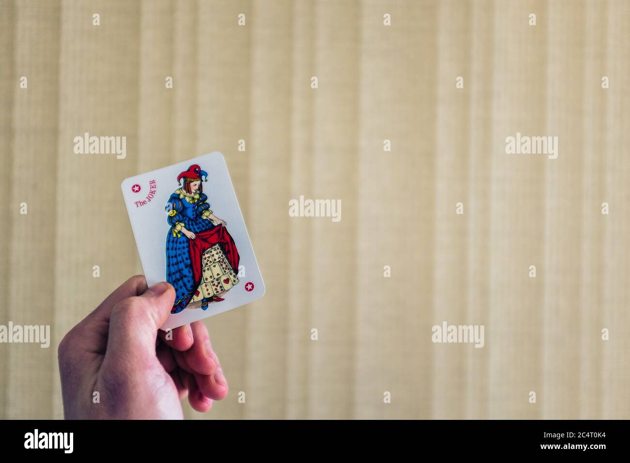 Closeup shot of a person holding the joker card behind a light background Stock Photo
