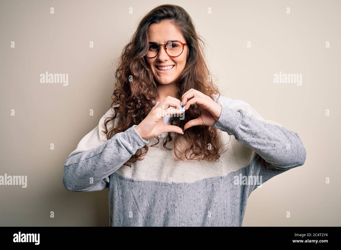 Young beautiful woman with curly hair wearing sweater and glasses over ...