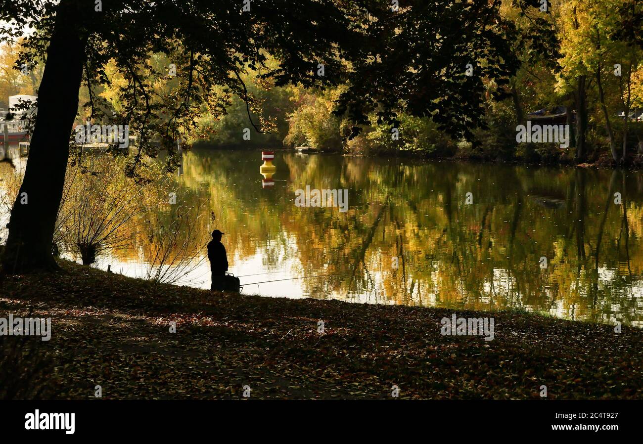 Angler on the riverbank with a reflection of autumnal trees in the water, colorful Stock Photo