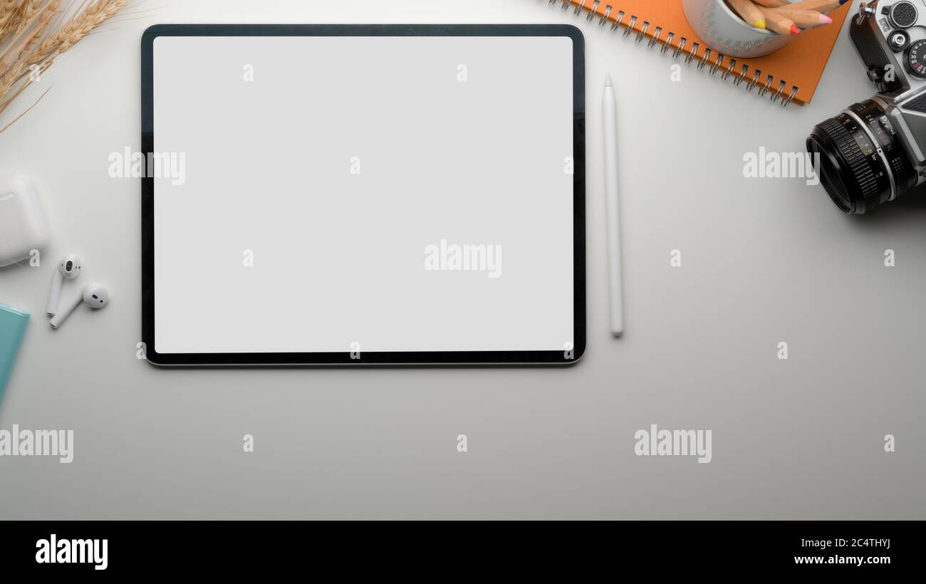 Top view of modern worktable with blank screen tablet, tea cup, camera, stationery and wireless earphone Stock Photo