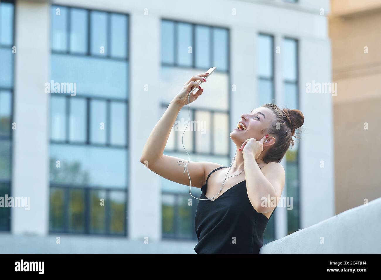beautiful girl poses in the city, holding a smartphone and listening to music with headphones. Stock Photo